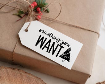 Può includere: Un regalo confezionato con un'etichetta bianca che recita "something you WANT" con una grafica di albero di Natale. Il regalo è avvolto in carta marrone e legato con spago e un rametto di bacche rosse.