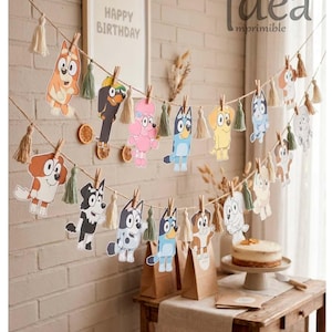 May include: A decorative party banner featuring multiple cartoon dog characters clipped onto two strands of twine with small wooden clothespins and interspersed with small beige and sage green fabric tassels, creating a festive display.