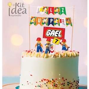 Puede incluir: Un pastel blanco con chispas de colores y un adorno de pastel con temática de Lego. El adorno presenta tres minifiguras de Lego, una pancarta que dice "Feliz Cumple" y un letrero que dice "Gael 7".