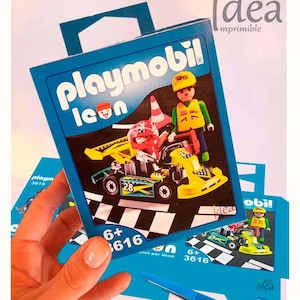 Puede incluir: Una caja azul de Playmobil con un kart amarillo y una figura. La caja muestra "Playmobil Icon" y "6+ 3616". La imagen también incluye unas tijeras azules.