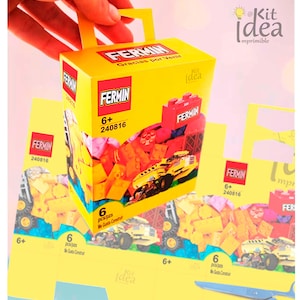 Puede incluir: Una caja amarilla con asa, que presenta un camión de construcción de juguete y el texto "FERMIN 240816". La caja está etiquetada "6+ pcs/pzs Me Gusta Construir" y tiene un logotipo de "Kit Idea". La caja es parte de un conjunto de favores de fiesta imprimibles.