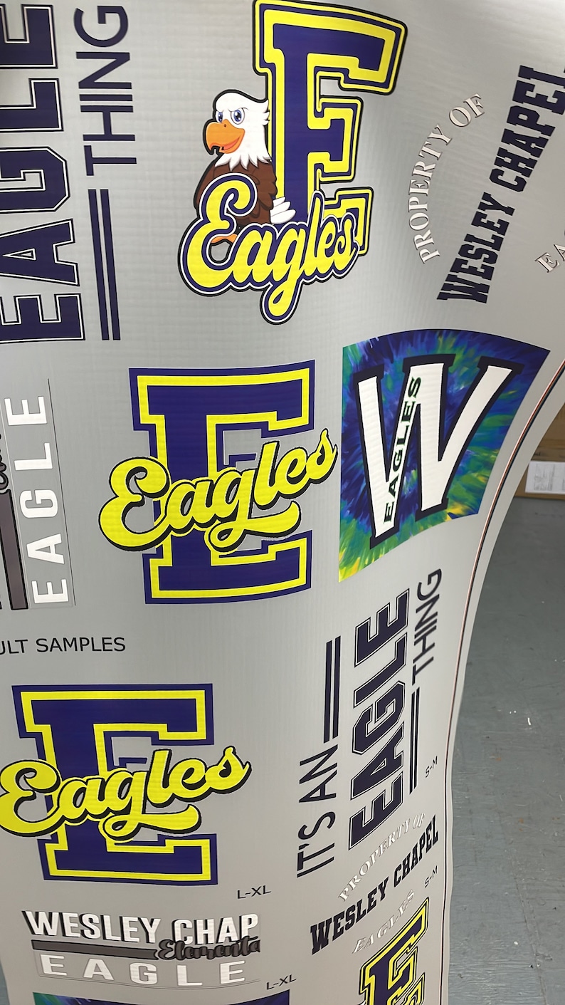 K&ouml;nnte beinhalten: Ein grauer Hintergrund mit einem blauen und gelben 'E' f&uuml;r Eagles-Logo. Das Logo wird in verschiedenen Gr&ouml;&szlig;en und Stilen wiederholt. Der Text 'Property of Wesley Chapel Eagles' ist ebenfalls sichtbar.