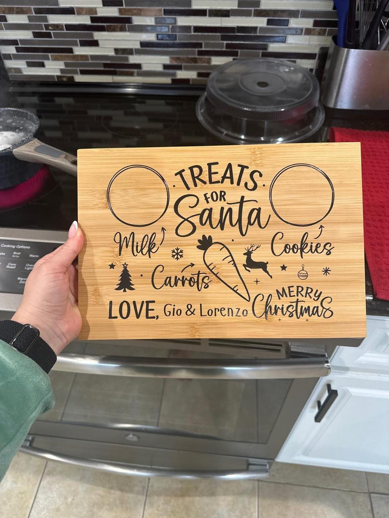 May include: A wooden chopping board with a Christmas theme. It has two circles for milk and cookies, and a space for carrots. The text reads "Treats for Santa, Milk, Carrots, Cookies, Merry Christmas, Love, Gio & Lorenzo".