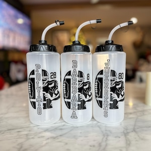 May include: Three clear plastic water bottles with black lids and straws. Each bottle has a black and white graphic of a football player with a number and a name: Polito 28, Barbara 8, and Juergens 80.