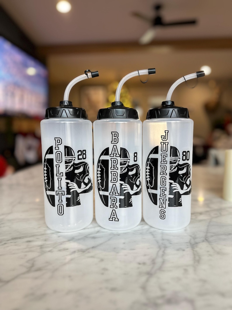 May include: Three clear plastic water bottles with black lids and straws. Each bottle has a black and white graphic of a football player with a number and a name: Polito 28, Barbara 8, and Juergens 80.