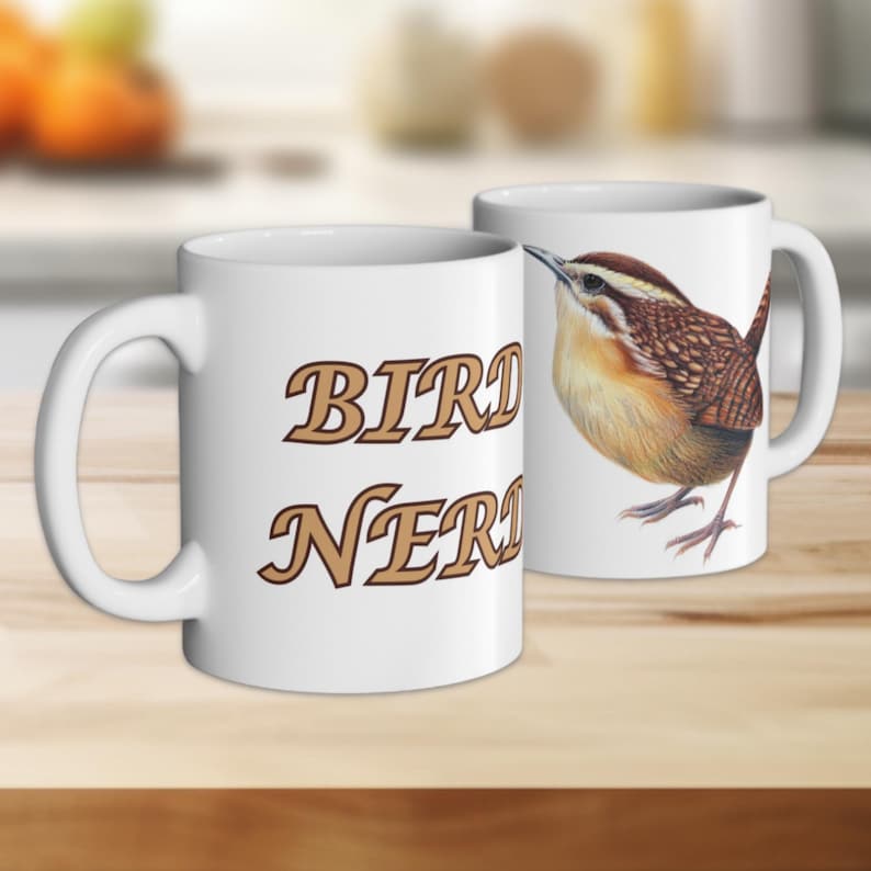 Puede incluir: Una taza de cer&aacute;mica blanca con el texto marr&oacute;n "BIRD NERD" en un lado y una ilustraci&oacute;n detallada de un peque&ntilde;o p&aacute;jaro choch&iacute;n de color marr&oacute;n y beige en el otro. La taza tiene un asa curva y un acabado exterior liso y brillante.