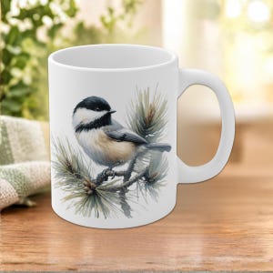 Puede incluir: Una taza de cerámica blanca con una ilustración detallada de un carbonero cabecinegro posado en una rama de pino. El ave tiene la cabeza y la garganta negras, mejillas blancas y el pecho de color tostado. Las agujas de pino son verdes.