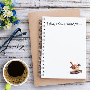 Carolina Wren profile vinyl sticker placed on a journal page on a desk. A coffee cup sits nearby in the scene