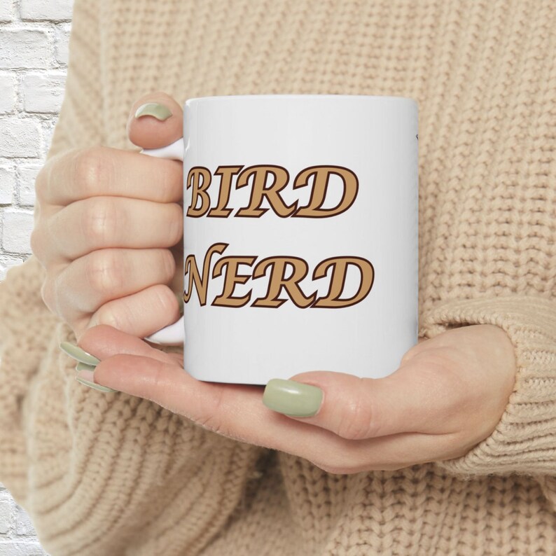 Puede incluir: Una taza de cer&aacute;mica blanca con el texto BIRD NERD impreso en una fuente serif marr&oacute;n en negrita. La taza tiene un cuerpo cil&iacute;ndrico liso con un asa en el lateral, dise&ntilde;ada para contener bebidas calientes o fr&iacute;as.