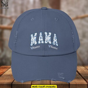 May include: A blue distressed baseball cap with the word "MAMA" in white letters with a floral pattern. The word "Name" is written below the word "MAMA" on each side of the cap.