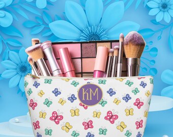 May include: A white zippered makeup bag with a colorful butterfly pattern and a purple circle with the initials "KM" in gold lettering.