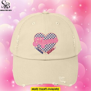 May include: A beige distressed baseball cap with a pink and blue checkered heart that says "Mama" in a pink retro font. The names "Caden" and "Olivia" are written below the heart.
