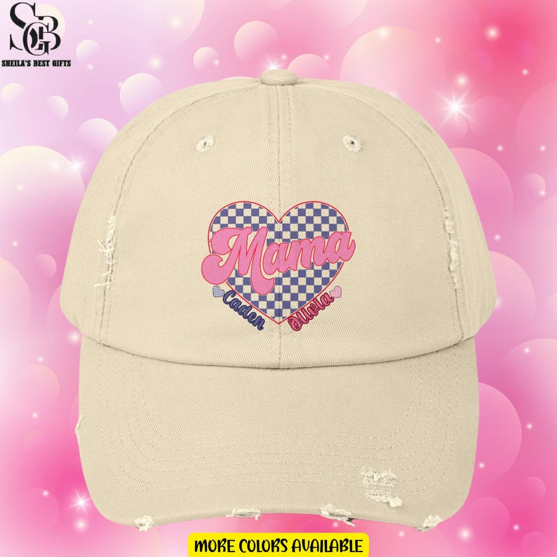 May include: A beige distressed baseball cap with a pink and blue checkered heart that says "Mama" in a pink retro font. The names "Caden" and "Olivia" are written below the heart.