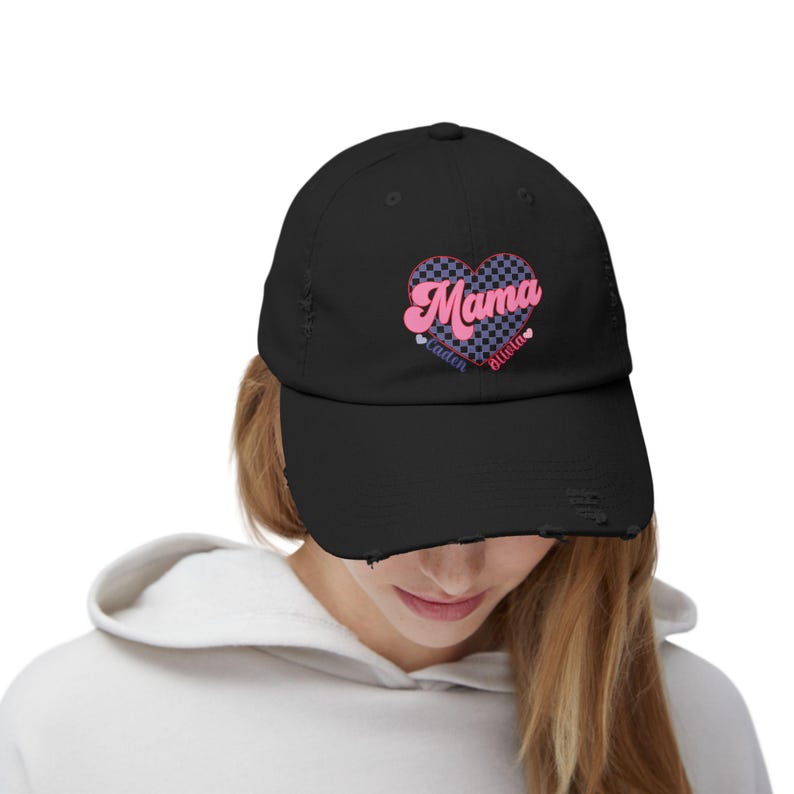 May include: Black distressed baseball cap with a pink and blue checkered heart that says "Mama" with the names "Caden" and "Briella" underneath.