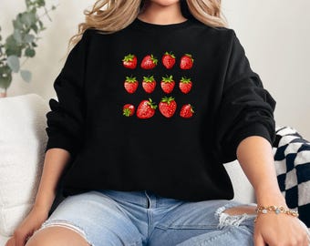 Peut inclure: Un sweat-shirt noir avec un motif de fraises rouges sur le devant. Les fraises sont disposées en grille.