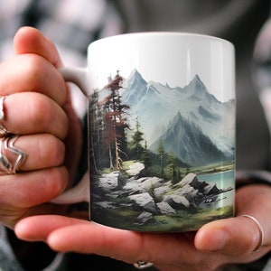 May include: White ceramic mug with a mountain scene printed on it. The scene features a lake, trees, and snow-capped mountains in the background.