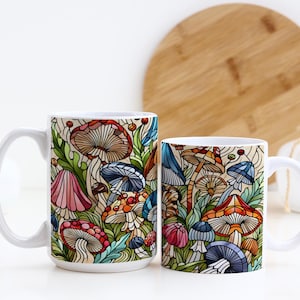 K&ouml;nnte beinhalten: Zwei wei&szlig;e Keramikbecher mit einem bunten Pilzdesign. Die Becher stehen auf einer wei&szlig;en Oberfl&auml;che mit einem Holzbrett im Hintergrund.