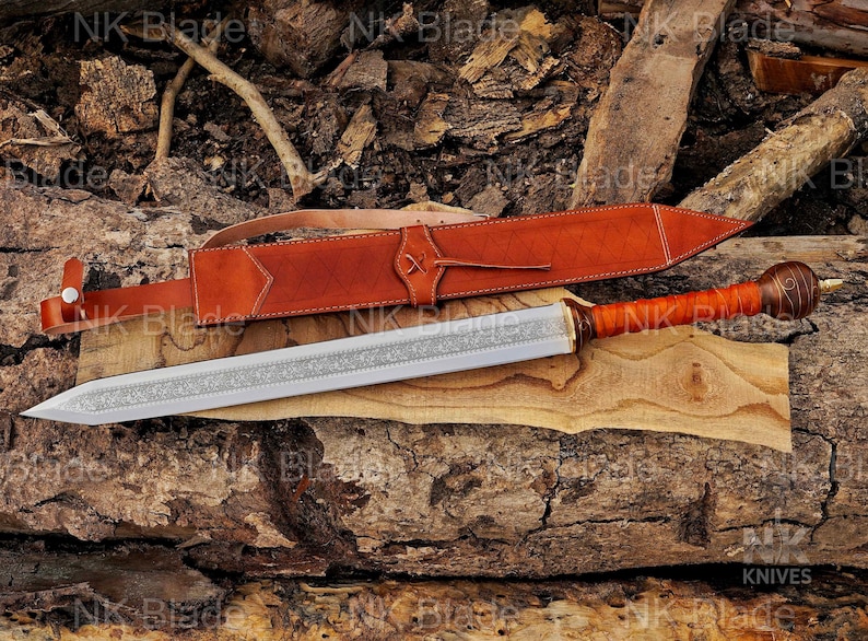 May include: A double-edged sword with a silver-toned blade featuring an intricate floral engraving along the center. The handle is wrapped in brown leather with a rounded pommel, accompanied by a matching brown leather sheath with white stitching.