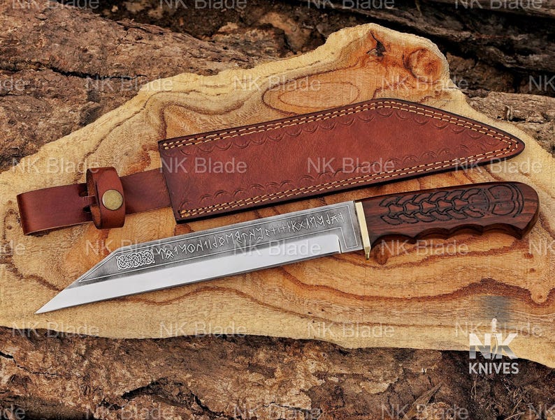 May include: A fixed-blade knife with a dark wood handle featuring carved knotwork patterns and a steel blade etched with runic inscriptions and Celtic designs. The knife includes a brown leather sheath with a belt loop and a brass-colored metal rivet.