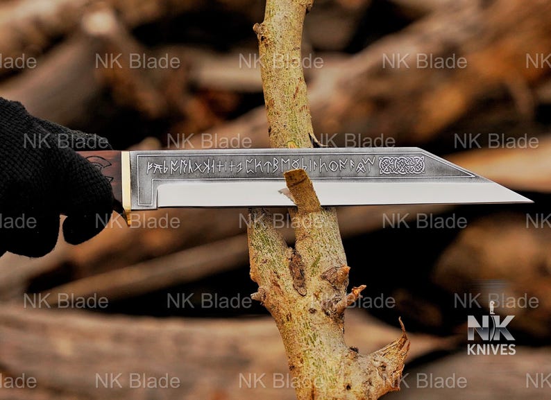 May include: A fixed-blade knife with a dark wooden handle and a metallic blade featuring etched runic inscriptions and a decorative knotwork pattern near the tip. The blade is positioned horizontally, cutting into a light brown tree branch.