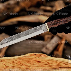 May include: A fixed-blade knife with a silver-toned steel blade featuring etched runic inscriptions and a decorative knotwork pattern near the hilt. The handle is crafted from dark brown wood with an intricate carved design and a brass-colored bolster.