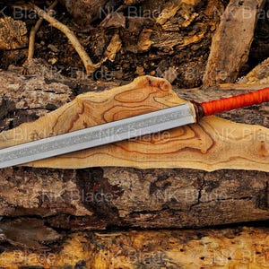May include: A double-edged sword with a silver-colored blade featuring an intricate etched pattern along the center. The handle is wrapped in bright orange cord and terminates in a dark brown, spherical pommel with a metallic tip.