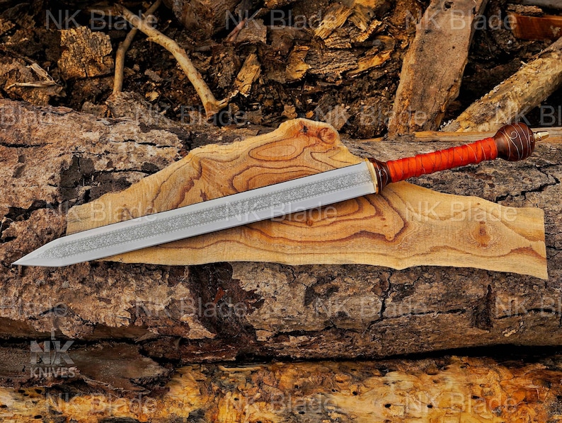 May include: A double-edged sword with a silver-colored blade featuring an intricate etched pattern along the center. The handle is wrapped in bright orange cord and terminates in a dark brown, spherical pommel with a metallic tip.