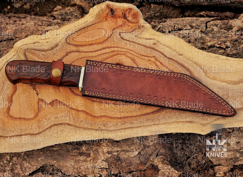 May include: A fixed-blade knife with a dark brown wooden handle featuring intricate carvings and a brass-colored snap button strap. The knife is encased in a brown leather sheath with decorative stitching along the edges and a textured surface.