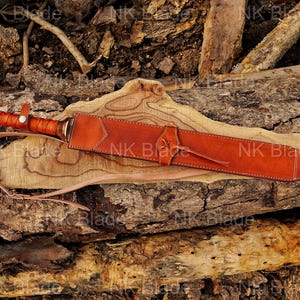 May include: A sword with a brown leather-wrapped handle and a spherical pommel, encased in a matching tan leather scabbard featuring stitched edges and a thin leather carrying strap. The text NK Blade is visible across the image.