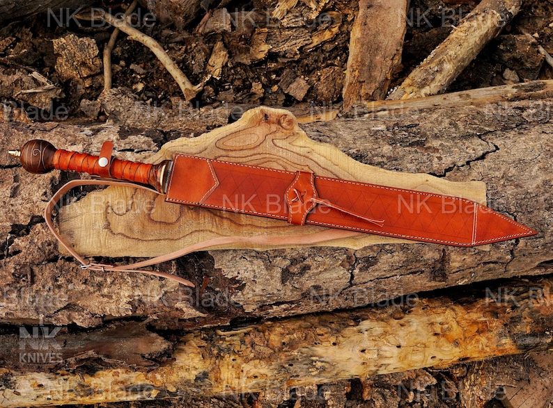 May include: A sword with a brown leather-wrapped handle and a spherical pommel, encased in a matching tan leather scabbard featuring stitched edges and a thin leather carrying strap. The text NK Blade is visible across the image.