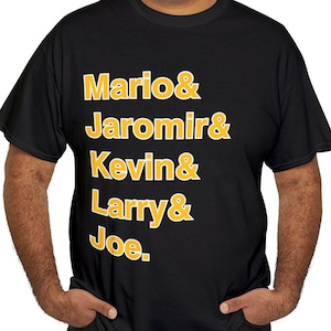 May include: A black t-shirt with a gold graphic print that reads "Mario & Jaromir & Kevin & Larry & Joe."