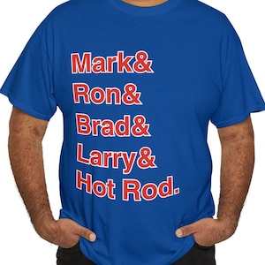 May include: A royal blue t-shirt with red text that reads "Mark & Ron & Brad & Larry & Hot Rod."