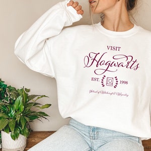 May include: White sweatshirt with a burgundy graphic that says "Visit Hogwarts Est. 1998 School of Witchcraft & Wizardry".