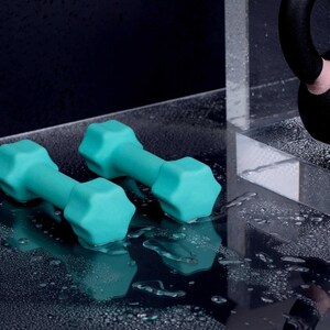 Puede incluir: Dos mancuernas de color turquesa sobre una superficie negra húmeda. Las mancuernas son de goma y tienen forma hexagonal.