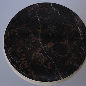 May include: A round black marble table top with brown veining. The table top is surrounded by a light beige rim.