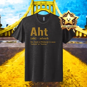 May include: A dark grey t-shirt with a gold print that says "Aht (aht) - adverb Out. Used in Pittsburgh to mean "outside" or "leaving."
