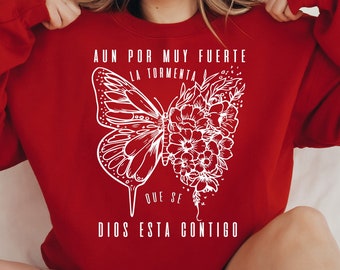 May include: Red sweatshirt with a white butterfly and floral design. The text "Aun por muy fuerte la tormenta que se Dios esta contigo" is printed on the sweatshirt.