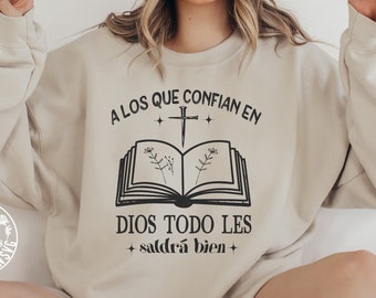 May include: A beige sweatshirt with a black graphic design that reads "A los que confian en Dios todo les saldra bien" with a cross and an open book with flowers.