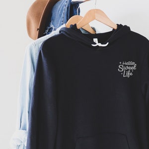 May include: Black hooded sweatshirt with a small white embroidered design that says "Hello Sweet Life" on the left chest.