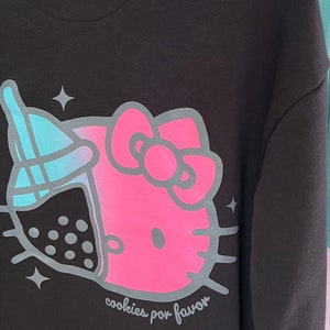 May include: Black hoodie with a pink Hello Kitty design and a blue and white boba tea graphic. The text "cookies por favor" is printed below the design.