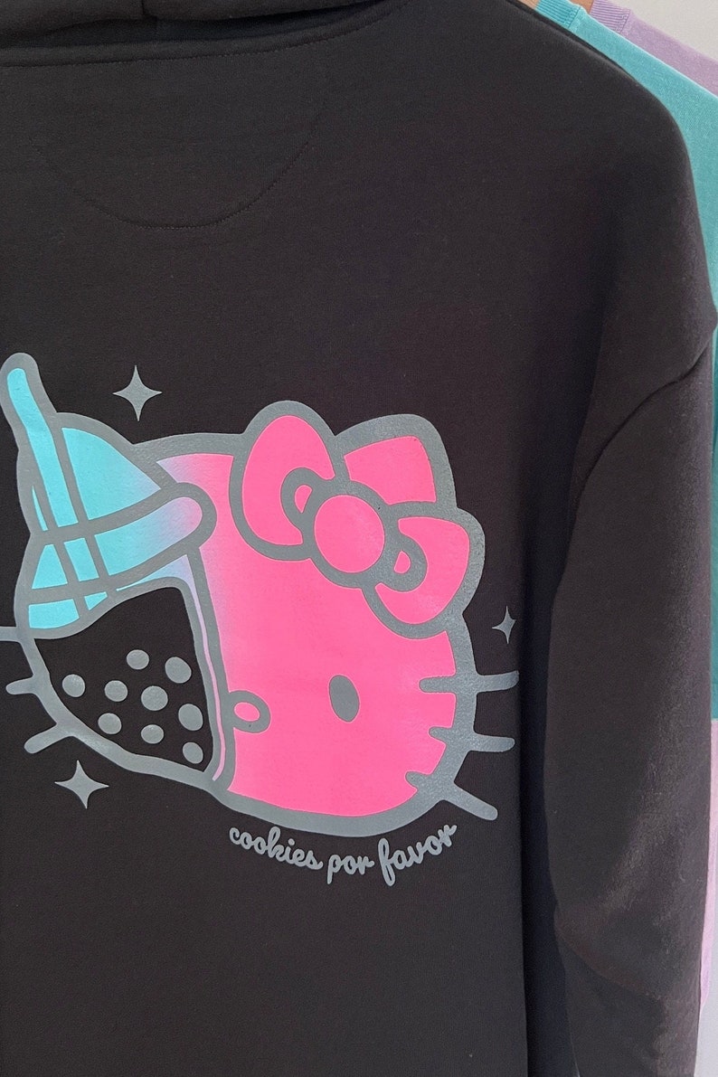 May include: Black hoodie with a pink Hello Kitty design and a blue and white boba tea graphic. The text "cookies por favor" is printed below the design.