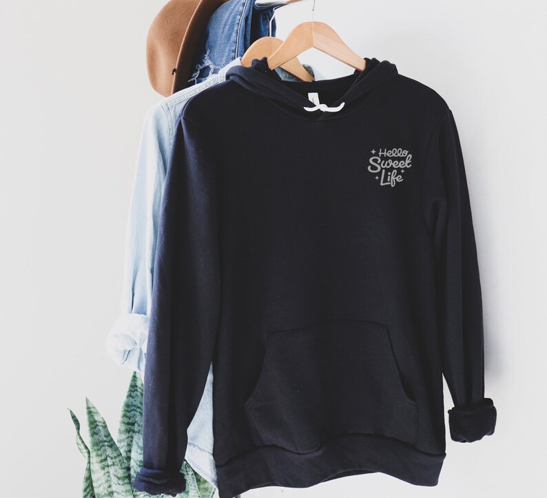 May include: Black hooded sweatshirt with a small white embroidered design that says "Hello Sweet Life" on the left chest.