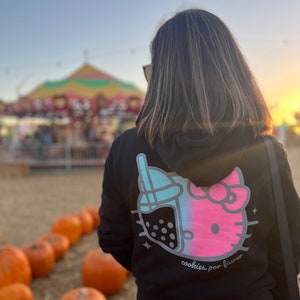 May include: Black hoodie with a pink and blue Hello Kitty and boba tea graphic on the back. The text "cookies por favor" is printed below the graphic.
