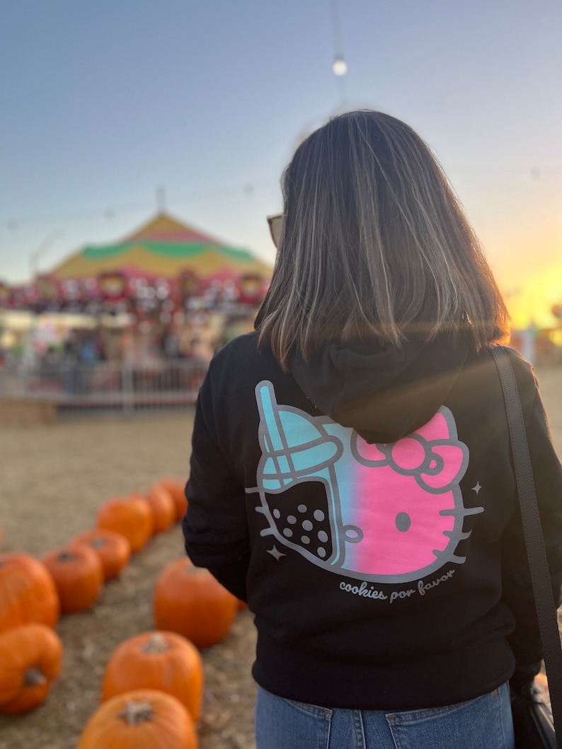 May include: Black hoodie with a pink and blue Hello Kitty and boba tea graphic on the back. The text "cookies por favor" is printed below the graphic.