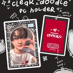 May include: A white and black illustrated design for a phone stand with a heart-shaped hole at the top and a rectangular hole at the bottom. The design includes the text "clear doodle PC holder" and "@cafetoyou".
