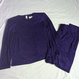 May include: A two-piece purple and black animal print outfit. The long-sleeved top has a keyhole back and the pants are gathered at the waist. The outfit is made of a soft, flowing fabric.