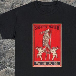 May include: Black t-shirt with a vintage-style illustration of a deer on a ladder with two cherubs on either side. The illustration is surrounded by a red border and the text "SAFETY MATCH" and "串田 絹 貢 製" in Japanese.