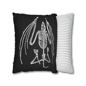 May include: Black pillow with a white skeletal bat illustration. The pillow has a white and gray striped pillowcase.