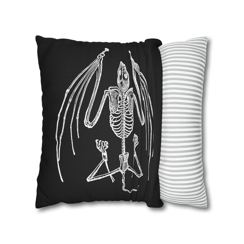 May include: Black pillow with a white skeletal bat illustration. The pillow has a white and gray striped pillowcase.