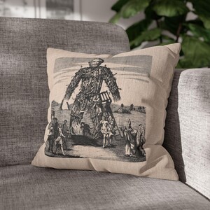 Könnte beinhalten: Eine Schwarzweißillustration einer großen, menschenförmigen Figur aus Ästen und Blättern. Die Figur ist von kleineren Figuren umgeben, von denen einige eine Leiter hinaufklettern. Die Illustration ist auf einem beigefarbenen Kissen gedruckt.